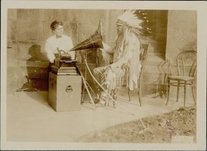 Mountain Chief, Chief of Montana Blackfeet, in Native Dress With Bow, Arrows, and Lance, Listening to Song Being Played On Phonograph and Interpreting It in Sign Language to Frances Densmore, Ethnologist, MAR 1916